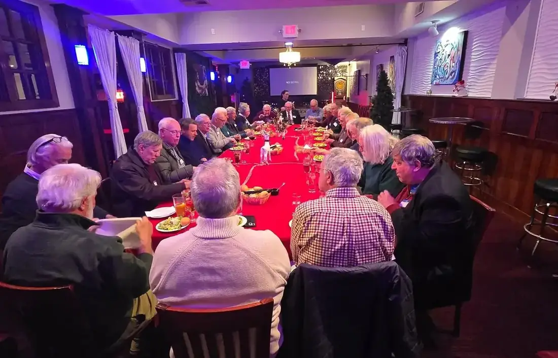 A long table of around twenty guests at a club dinner on the first floor at Midtown Social, with name badges and a projection screen at the end of the room.