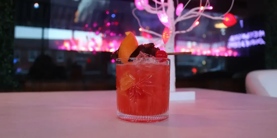 A red signature cocktail with orange, cherry and cinnamon garnish on the bar at Midtown Social.