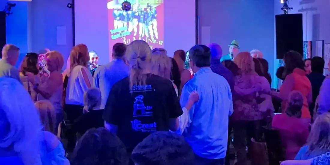 A packed dance floor at a 30 Main event, the band's poster projected on the wall behind the crowd.