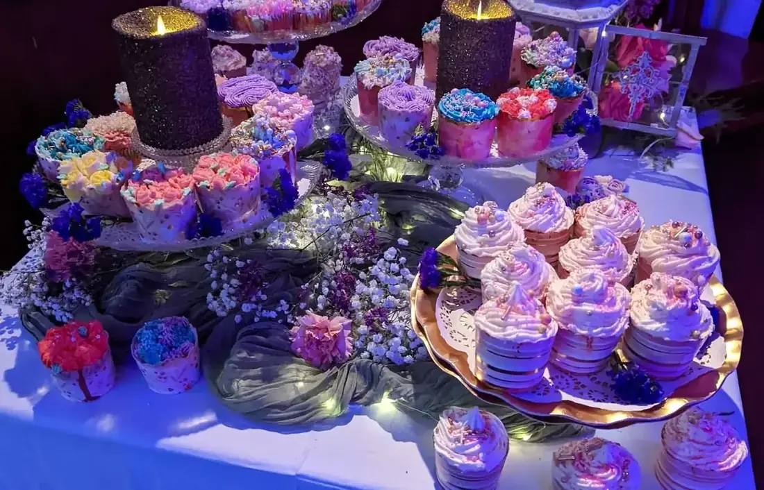 A dessert station of iced cupcakes on tiered stands with candles, greenery and fresh flowers.