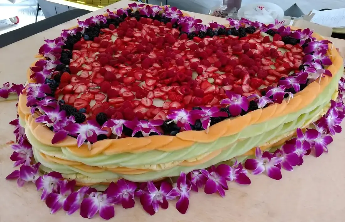 A large fruit display built from sliced melon, strawberries, raspberries and blackberries, edged with purple orchids.
