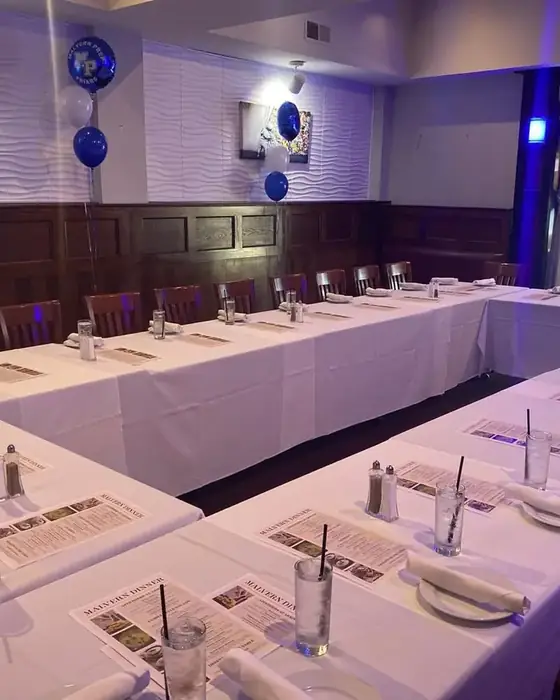 Long banquet tables in white linen set for a school dinner with printed menus and balloons.