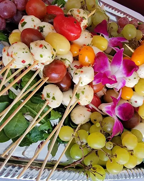 Caprese skewers with marinated mozzarella and heirloom tomatoes on a silver tray with grapes.