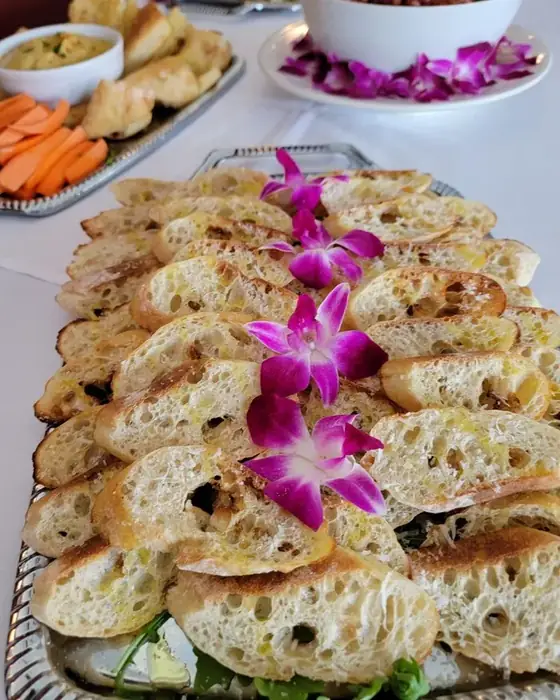 A silver tray of grilled crostini dressed with orchids, with hummus and crudite alongside.