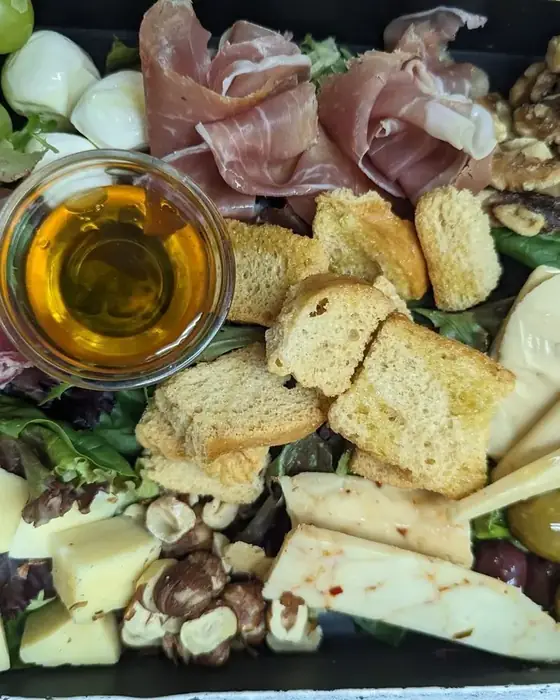 A charcuterie board with prosciutto, salami, aged cheeses, walnuts, olives, grapes and honey.