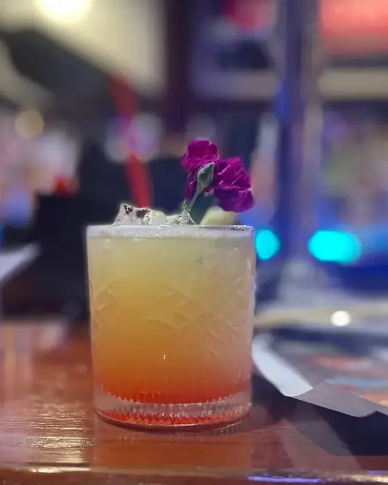 An amber layered cocktail garnished with a purple flower on the bar.