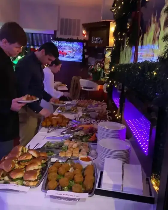 A labelled catering buffet at a corporate holiday party with short rib sliders and vegetarian arancini.