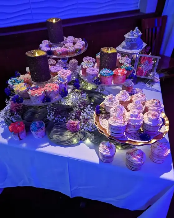 A dessert station of iced cupcakes on tiered stands with candles and fresh flowers.