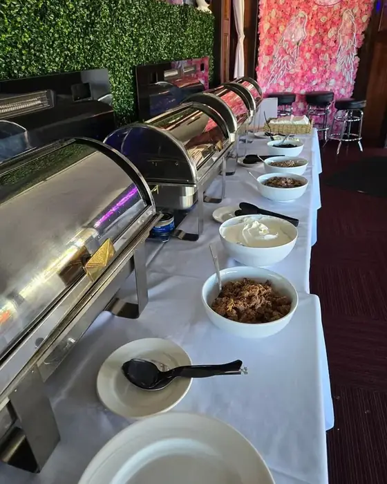 A carving station and buffet beside the pink flower wall with neon angel wings at Midtown Social.