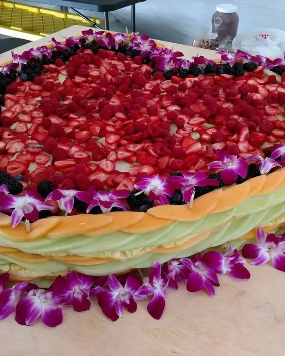 A large fruit display of melon, strawberries and berries edged with purple orchids.