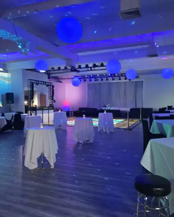 Midtown Hall set with cocktail tables, hanging lanterns, blue uplighting and a lit dance floor.
