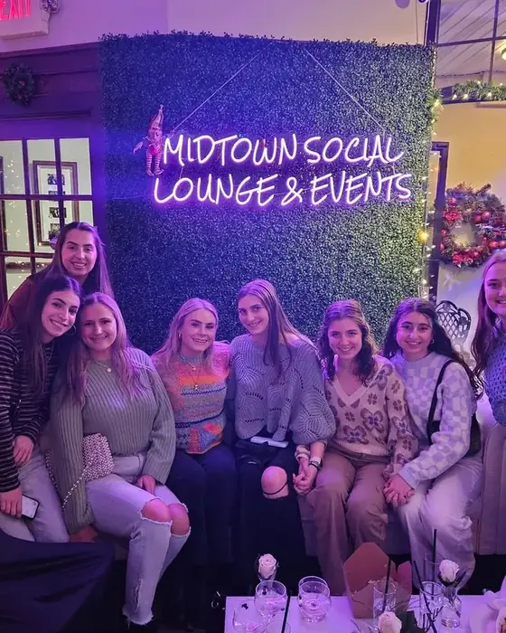 A group of friends at the neon wall at Midtown Social surrounded by Christmas decorations.