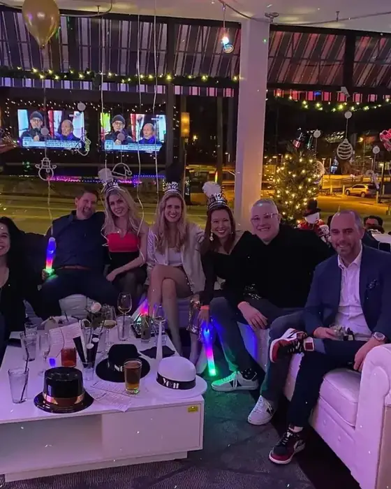 Friends in party hats on the white sofas at Midtown Social on New Year's Eve, with Christmas trees and an Eagles flag behind.