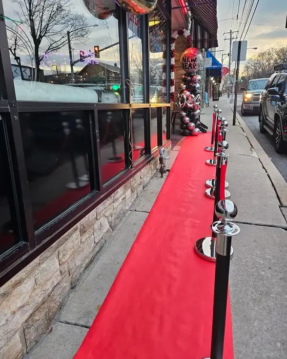 A red carpet and stanchions along the sidewalk outside Midtown Social on Lancaster Avenue with balloon columns at the door.