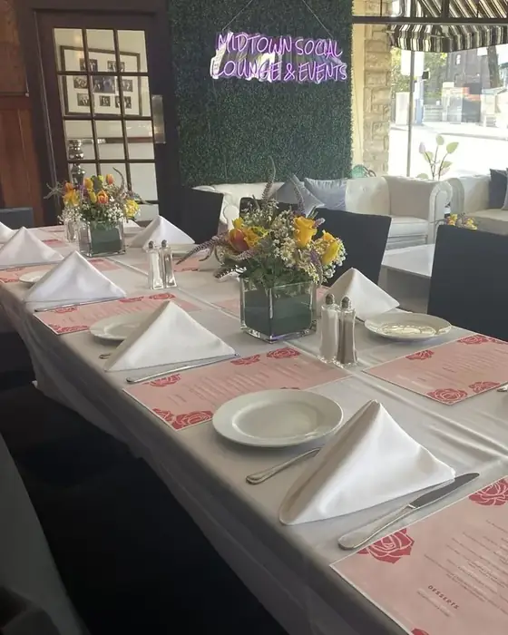 A shower table set with white linen, rose-printed menus and spring flowers beside a flower wall.
