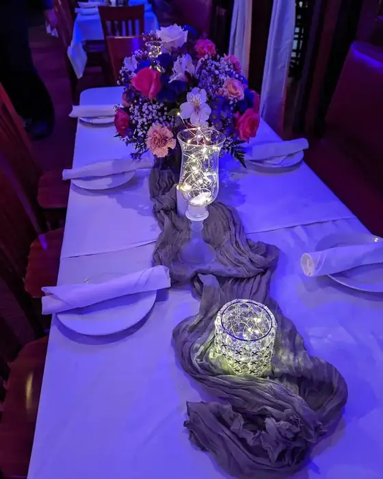 A long table styled with a cheesecloth runner, fairy lights in glass hurricanes and a floral centrepiece.