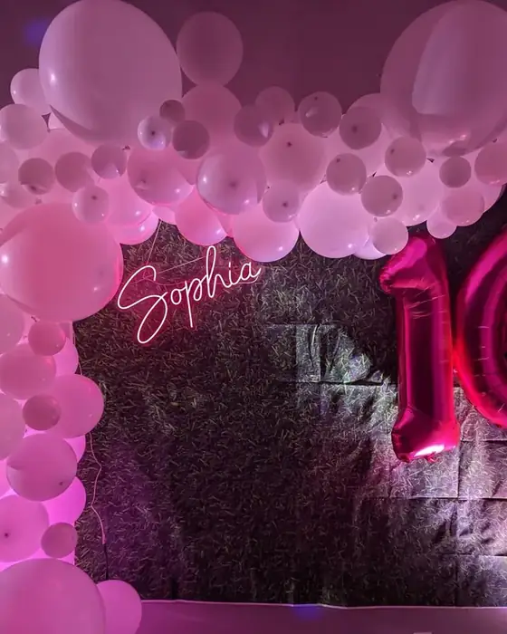 A pink and white balloon arch with a personalised neon name sign and giant number sixteen balloons for a sweet sixteen.