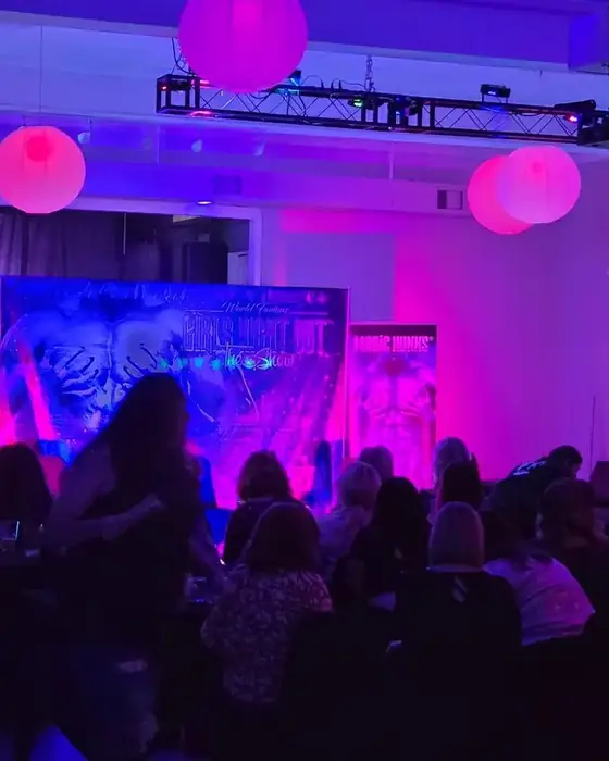 A full seated audience in Midtown Hall watching a ticketed touring show under pink lighting.