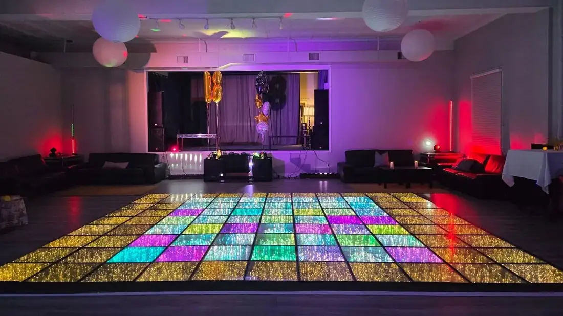 Midtown Hall with the LED dance floor lit in rainbow colours, lounge seating around the edges, the stage at the far end and truss lighting overhead.
