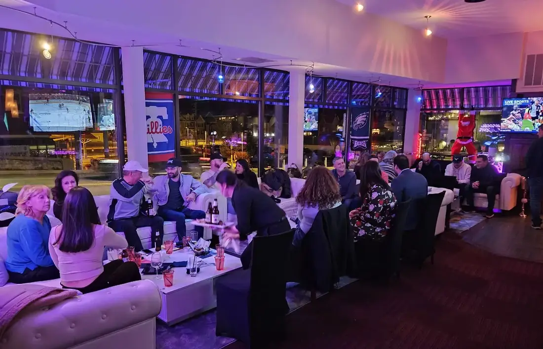 Big screens showing hockey and UFC above the lounge at Midtown Social, with Phillies and Eagles flags hanging in the windows and guests on the sofas.